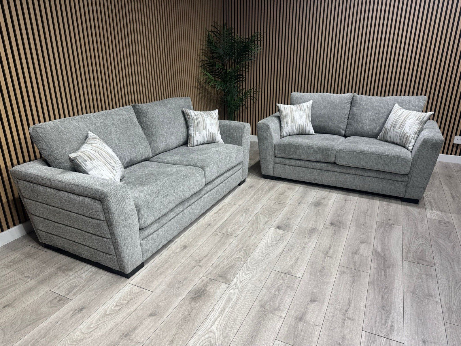 Two gray sofas with patterned cushions in a room with wooden flooring and wall.