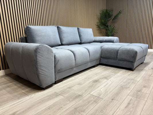 Gray sectional sofa in a room with wooden flooring and a slatted wall.