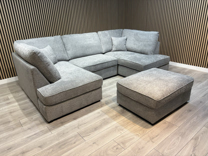 Gray sectional sofa with ottoman on a wooden floor against a wooden paneled wall.