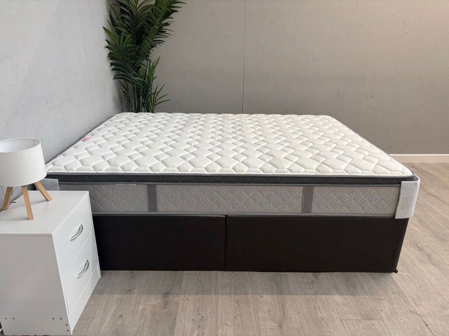 White mattress on a black frame with a plant and white cabinet in the background.