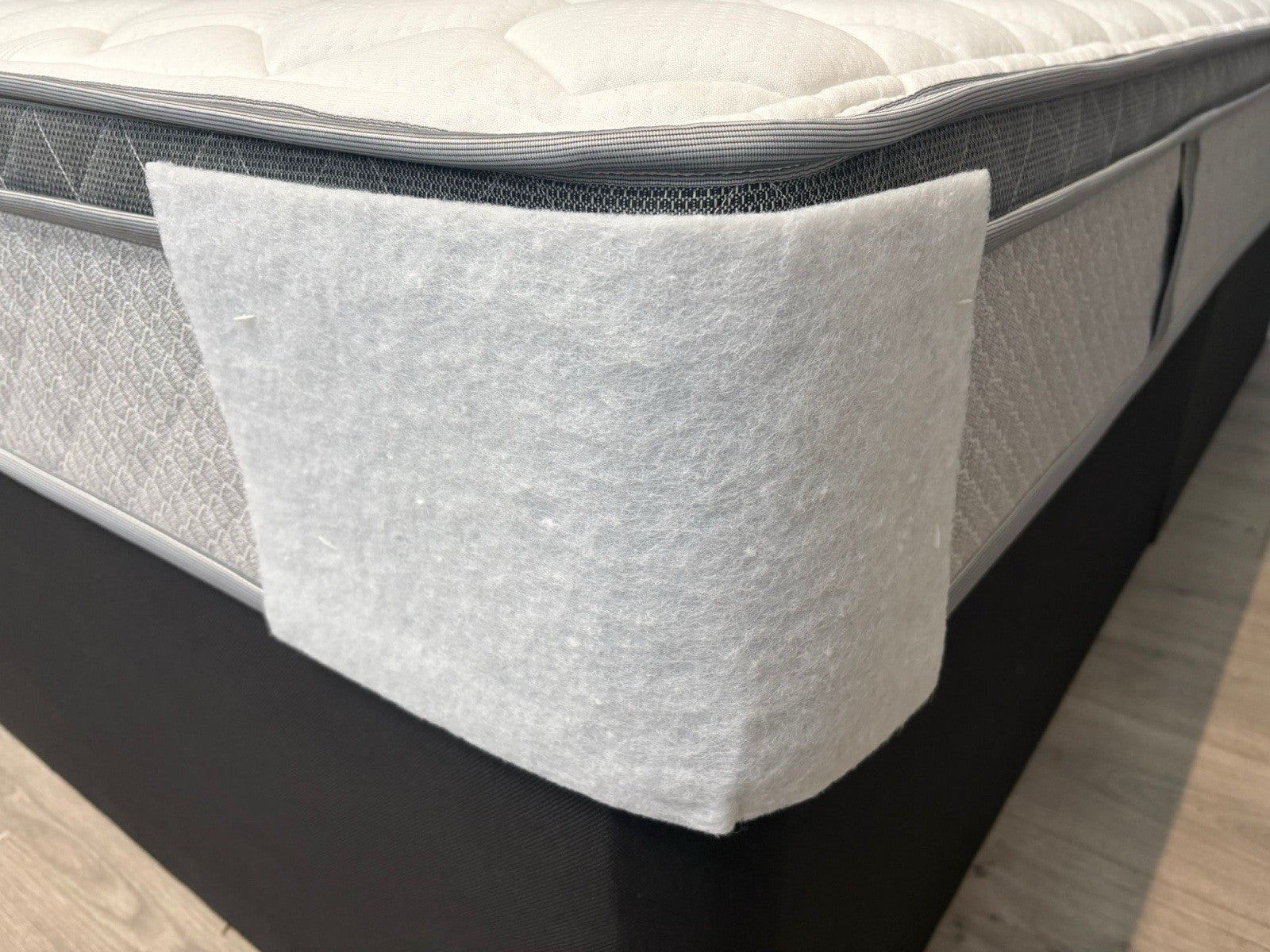 Gray mattress topper on a bed with a wooden floor in the background