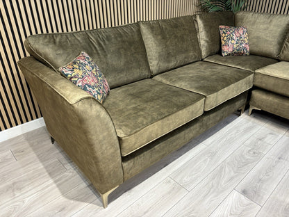 Green sectional sofa with floral cushions on a wooden floor.