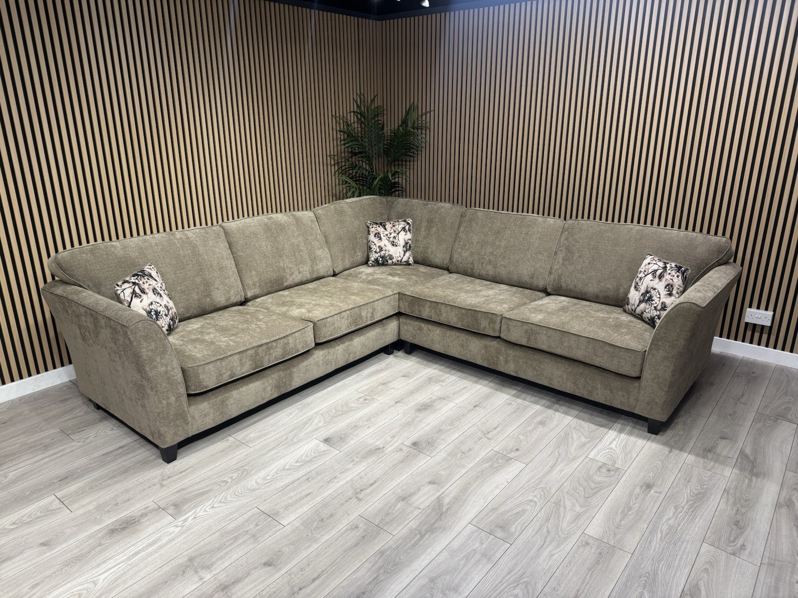 Brown sectional sofa with patterned cushions in a room with wooden walls and floor.