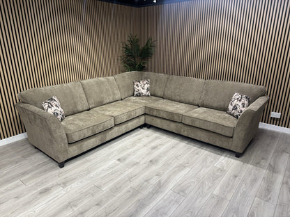 Brown sectional sofa with patterned cushions in a room with wooden walls and floor.