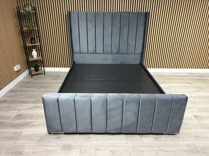 Gray upholstered bed in a room with wooden flooring and a wall.