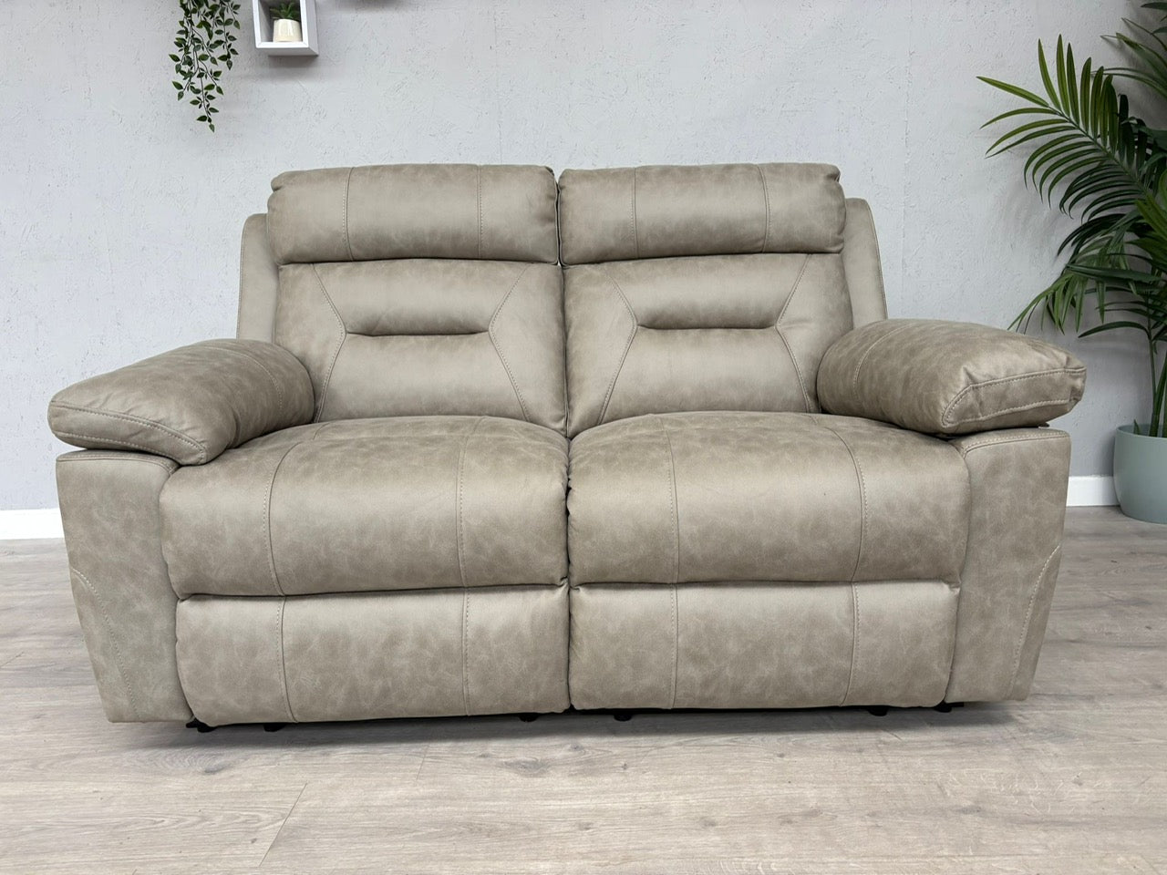 Beige reclining sofa in a room with plants and a light gray wall.