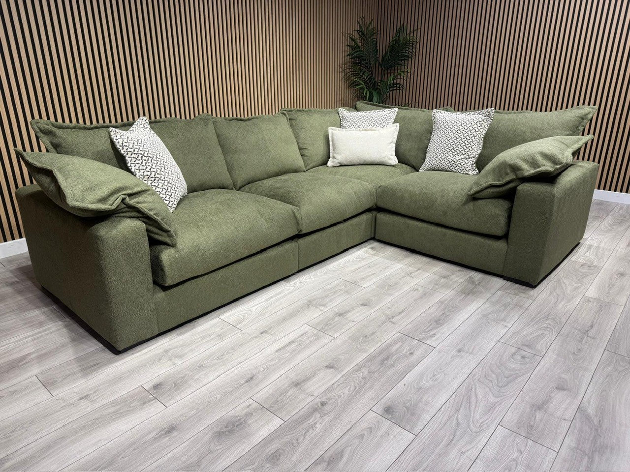 Green sectional sofa with patterned cushions on a wooden floor.