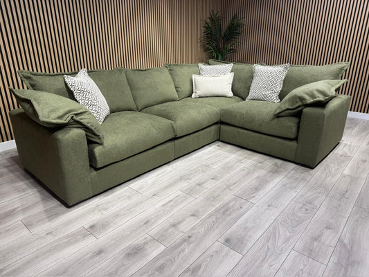 Green sectional sofa with patterned cushions on a wooden floor.